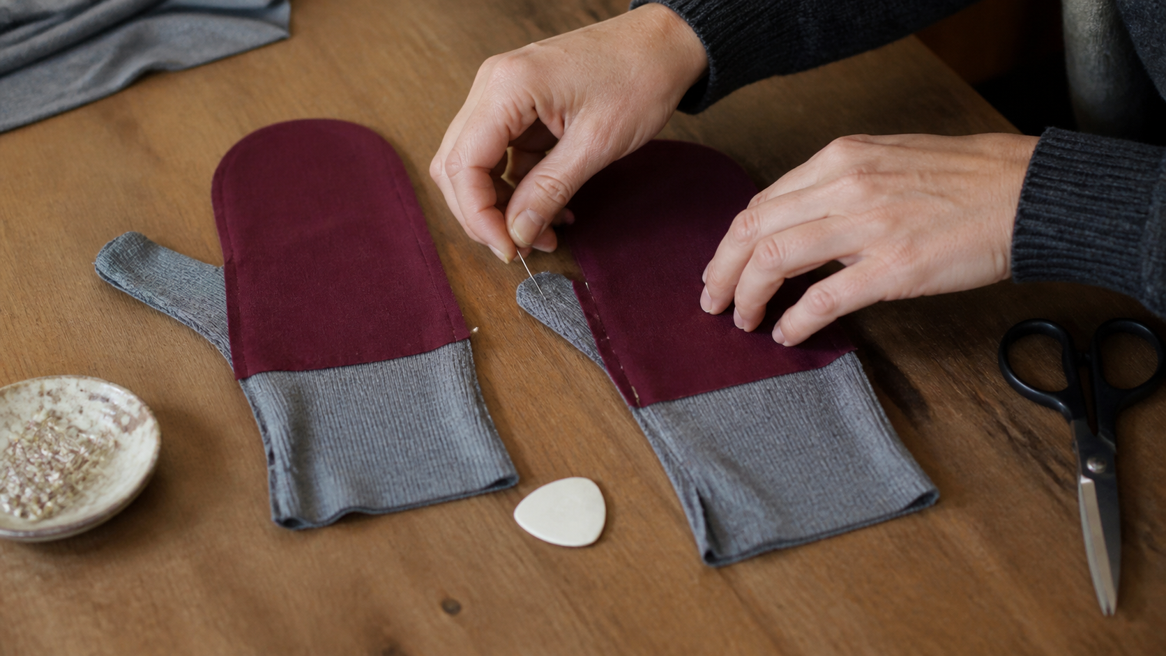 Paire de mitaines en tissu extensible en cours de couture sur un plan de travail avec patron, épingles et machine à coudre.